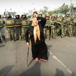 #46 Chinese Riot Police Watch A Muslim Ethnic Uighur Woman Protest In Urumqi In China’s Far West Xinjiang Province Following A Third Day Of Unrest, 7 July 2009